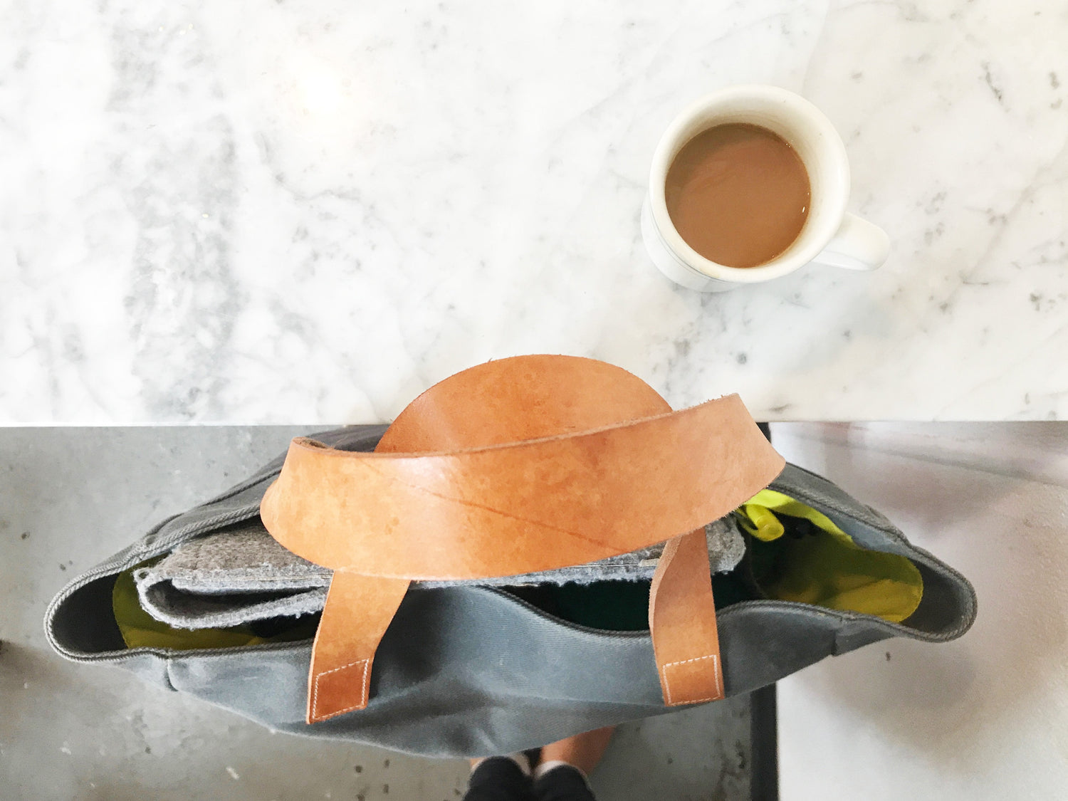 The Morning Person, the charcoal laptop bag, featured at a coffeeshop with a cup of coffee. 